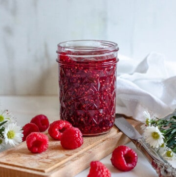raspberry jam in a small glass jar with a light colored background